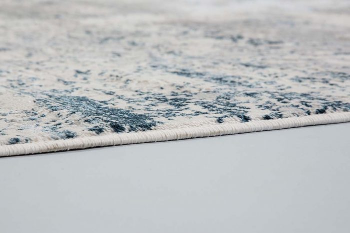 Rechteckiger Kurzflorteppich in blau-grauem Muster mit beiger Stoffkante