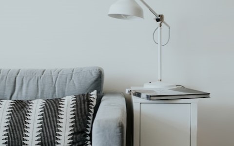 Graues Stoffsofa mit schwarz-weiß gestreiftem Kissen und einem weißen Beistelltisch mit Lampe und Buch