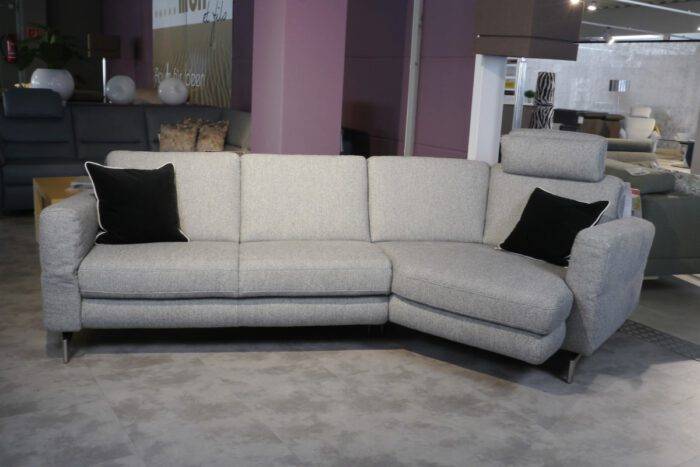 Graues Stoffsofa mit Trapezecke und einer Kopfstütze. Die Metallfüße sind matt satiniert.
